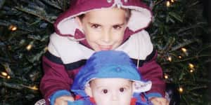 Jona and his brother pose in front of a Christmas tree.